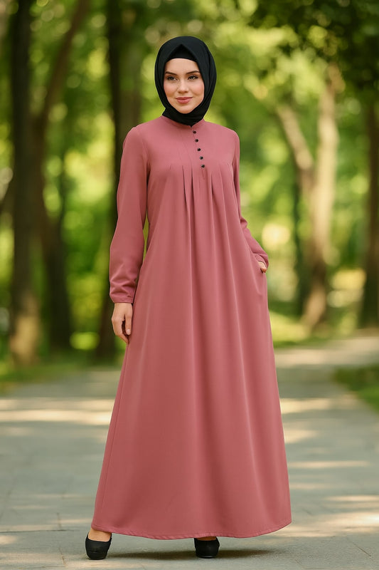 Woman wearing a long pink dress and black hijab standing in a park.