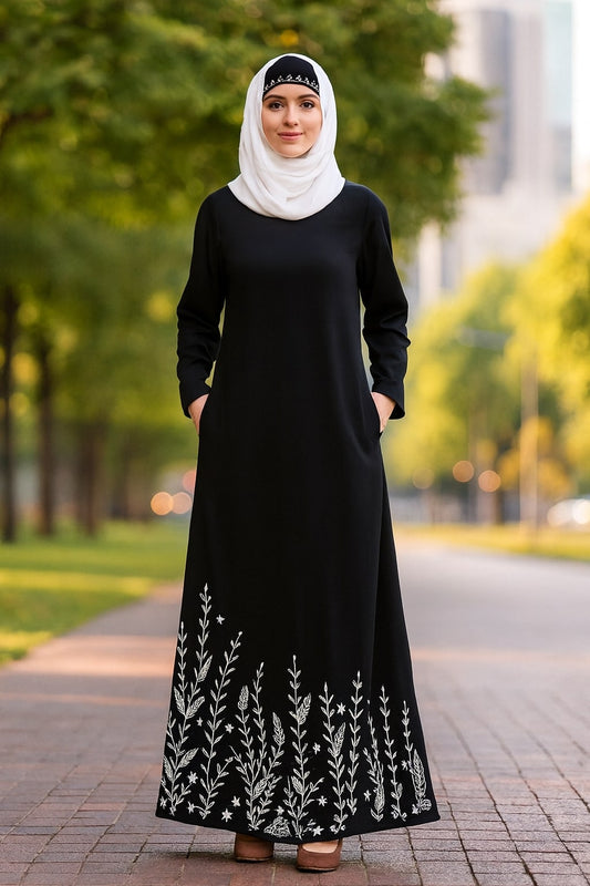 Woman wearing a black dress with white floral embroidery in an outdoor setting.