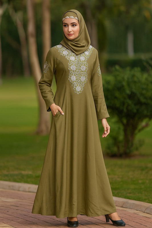 Woman wearing an olive green dress with white embroidery in a park setting