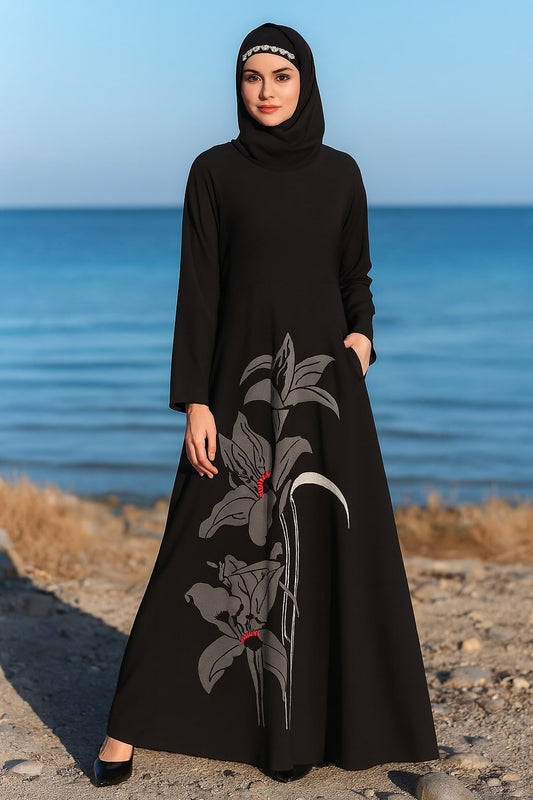Woman in a black dress with floral patterns standing by the ocean.