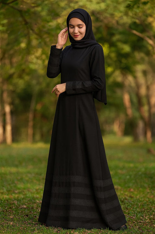 Woman wearing a black dress and hijab standing in a park with greenery.