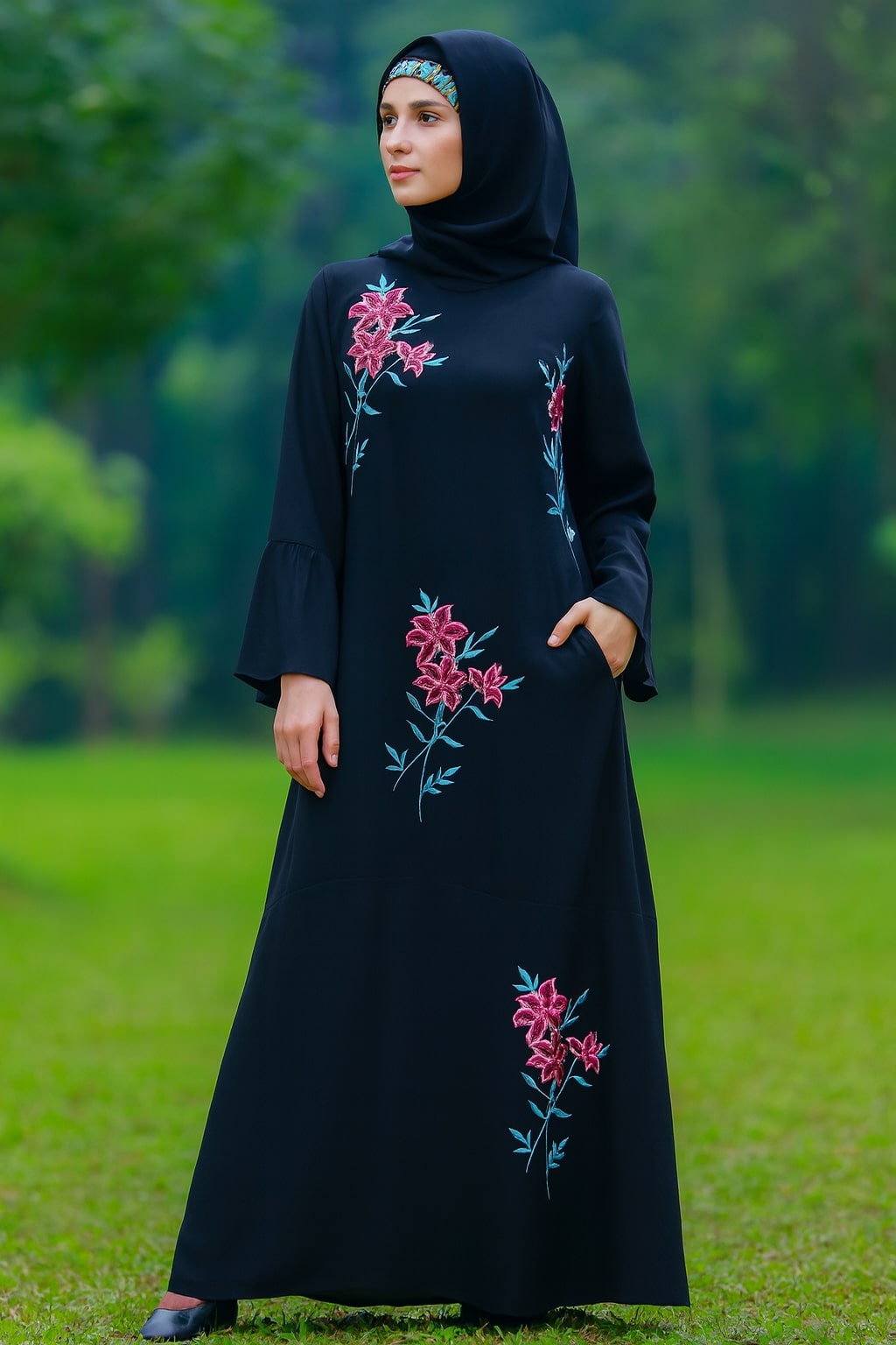 Woman wearing a black dress with floral embroidery standing in a green outdoor setting