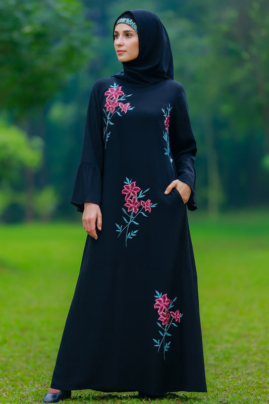 Woman wearing a black dress with floral embroidery standing in a green outdoor setting