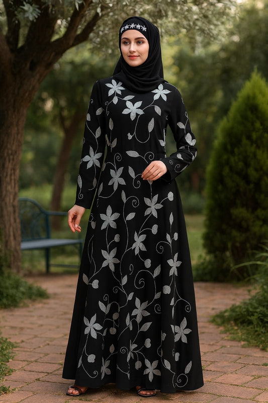 Woman wearing a black abaya with white floral patterns in an outdoor setting.