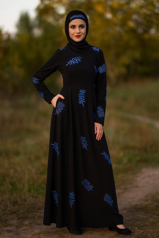 Woman wearing a black dress with blue patterns standing outdoors.