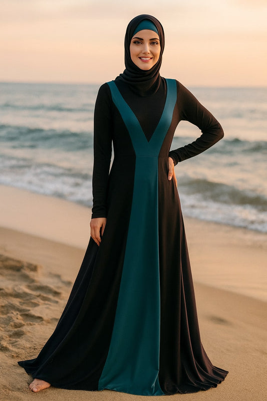 Woman in a black and teal abaya standing on a beach at sunset.