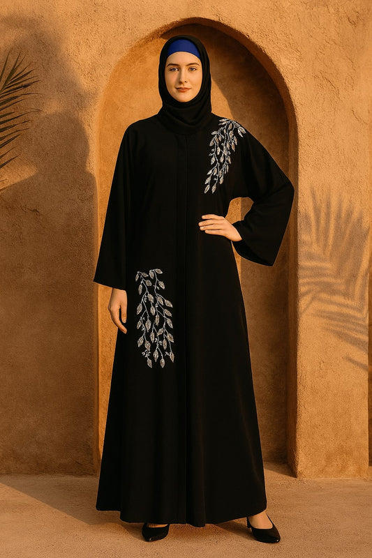 Woman wearing a black abaya with white embroidery in front of a sandy archway.