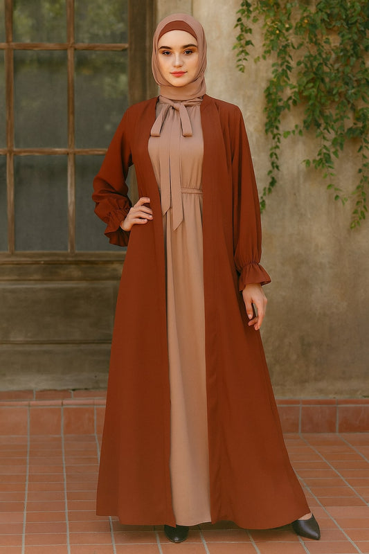 Woman wearing a brown and beige dress with a matching hijab against a rustic wall.