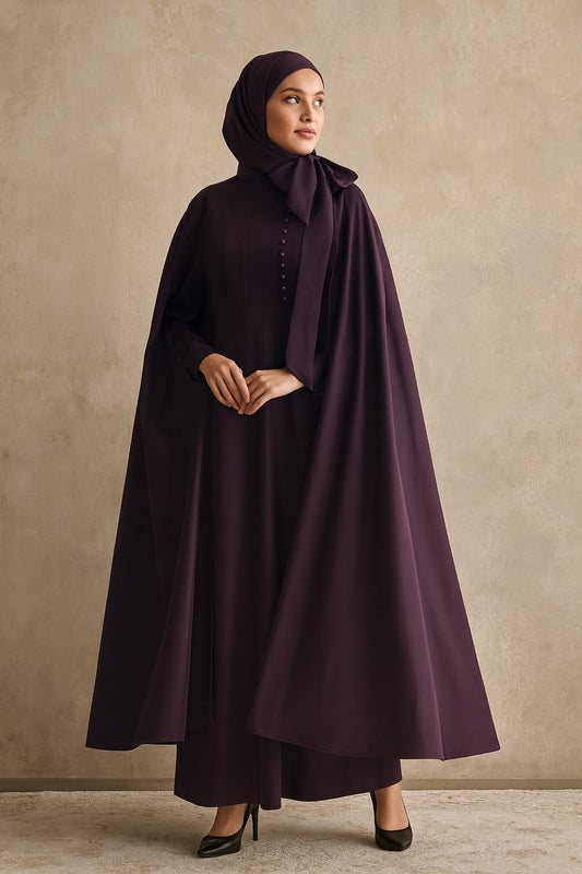 Woman wearing a dark purple outfit with a cape against a beige background