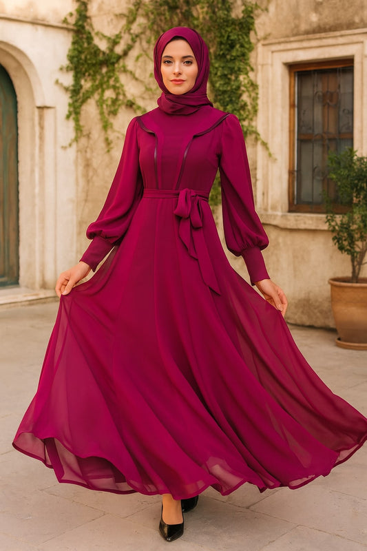 Woman in a long, flowing magenta dress with a matching hijab standing outdoors.