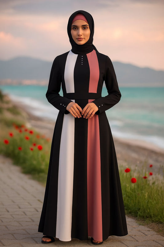 Woman wearing a long, black dress with colorful stripes standing on a path by the sea.