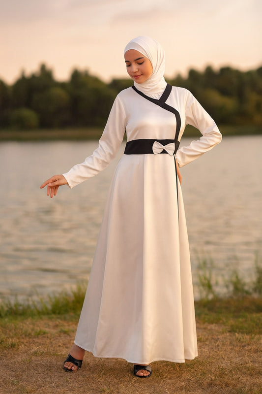Woman in a white dress with black accents standing by a body of water.
