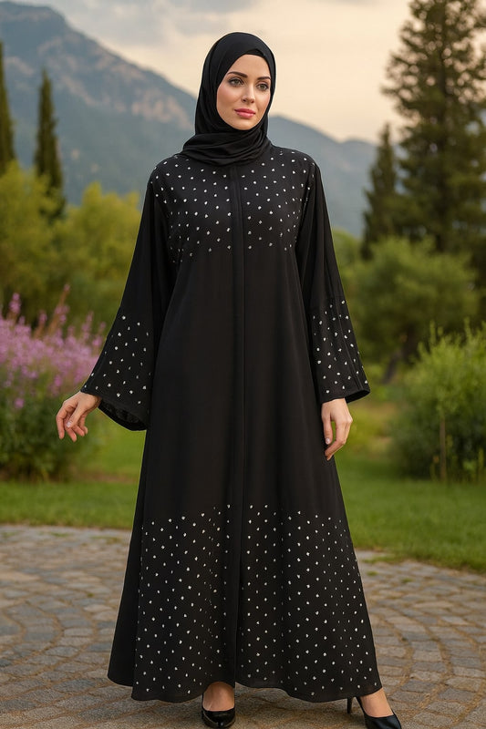 Woman wearing a black dress with white patterns in an outdoor setting with greenery and mountains.