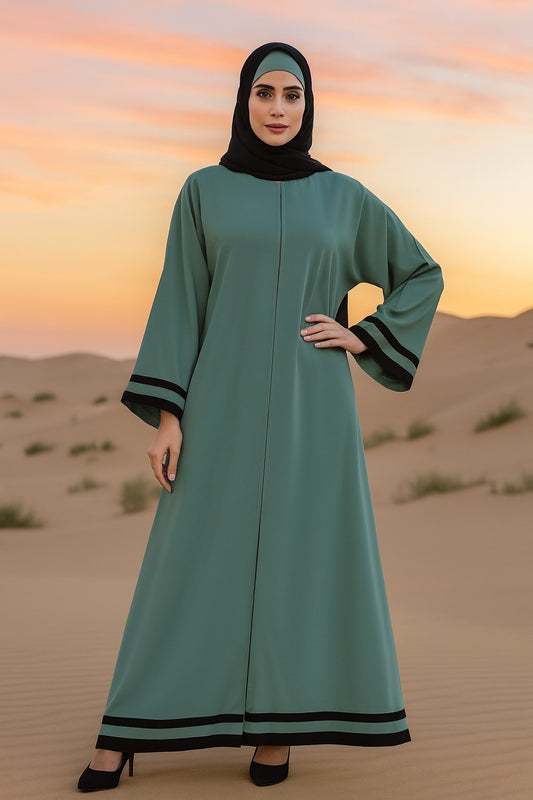 Woman in a teal dress with black trim standing in a desert landscape at sunset.