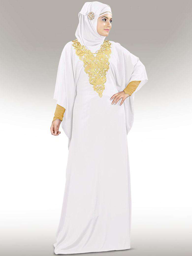 A woman wearing a white kaftan with gold embroidery at the neckline and a square hijab.