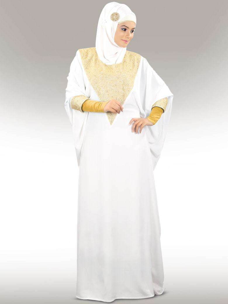 A woman wearing a white kaftan with golden bead hand embroidery around the neckline and cuffs, standing against a plain background.