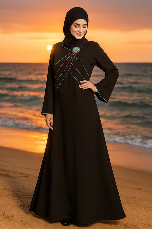 Woman in a black dress with a hijab standing on a beach at sunset.