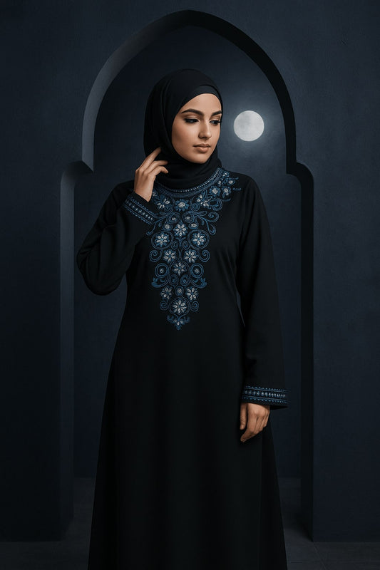Woman wearing a black abaya with blue embroidery in a dark setting