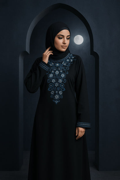 Woman wearing a black abaya with blue embroidery in a dark setting