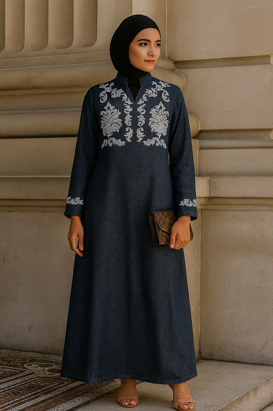 Woman wearing a dark blue dress with white embroidery against a beige wall.