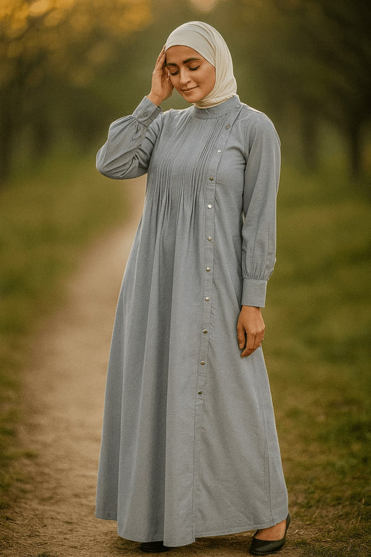 Woman wearing a long gray dress with a hijab standing on a path in a natural setting.