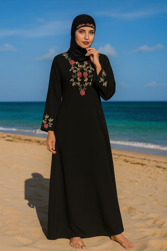 Woman in a black dress with floral embroidery standing on a beach.