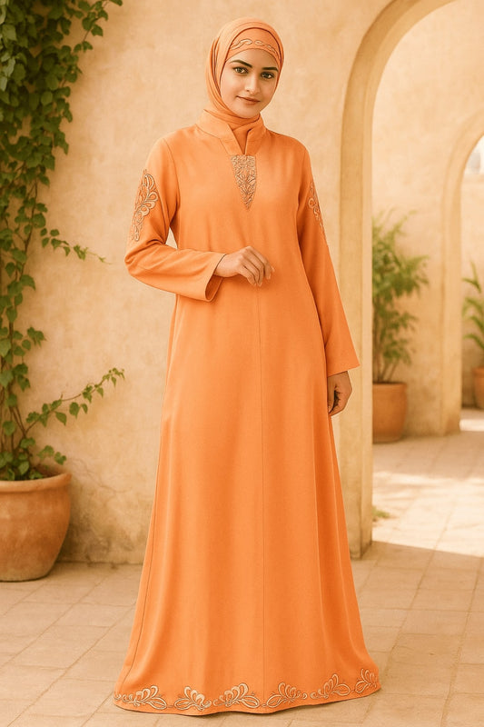 Woman wearing an orange abaya with intricate designs in a warm-toned outdoor setting.