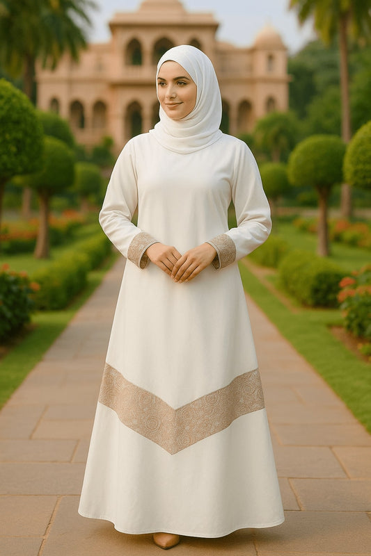 Woman in a white dress with a beige pattern standing on a pathway with greenery and a building in the background.