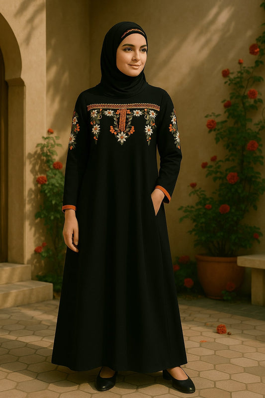 Woman wearing a black embroidered dress standing outdoors with plants and flowers in the background.
