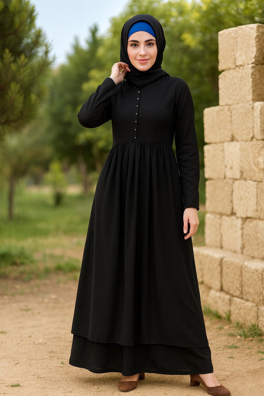 Woman wearing a black dress with a blue headscarf standing outdoors near stacked stones.
