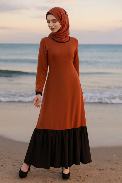 Woman wearing an orange and black dress standing on a beach at sunset.