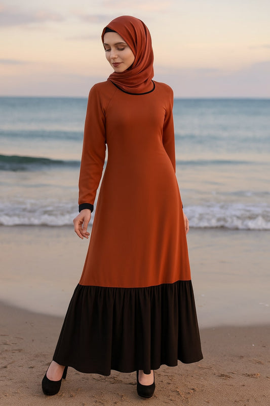Woman wearing an orange and black dress standing on a beach at sunset.