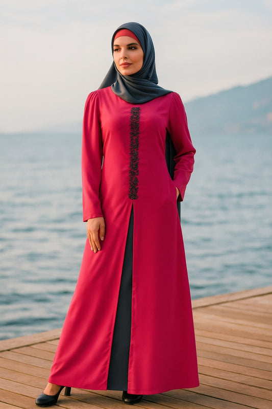 Woman in a pink dress with a black hijab standing on a wooden dock by water.