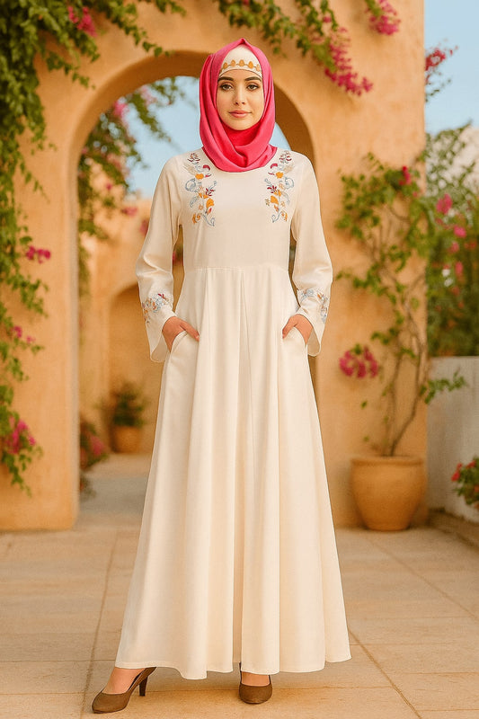 Woman in a long, embroidered cream dress with a pink hijab standing in front of an archway with floral decorations.
