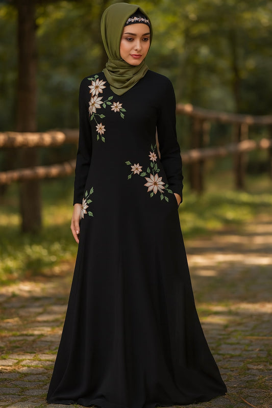 Woman wearing a black dress with floral patterns and a green hijab in a natural setting.