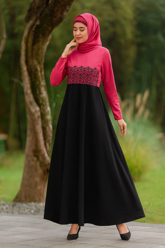 Woman wearing a pink top and black dress with a hijab, standing outdoors.