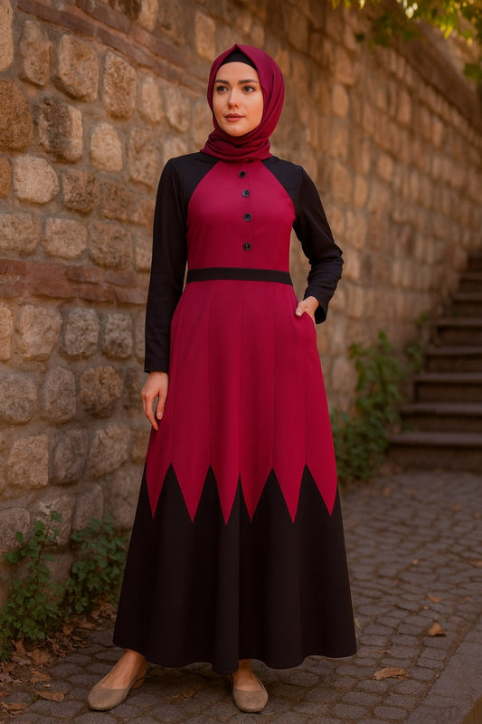 Woman wearing a red and black dress with a hijab standing against a stone wall.