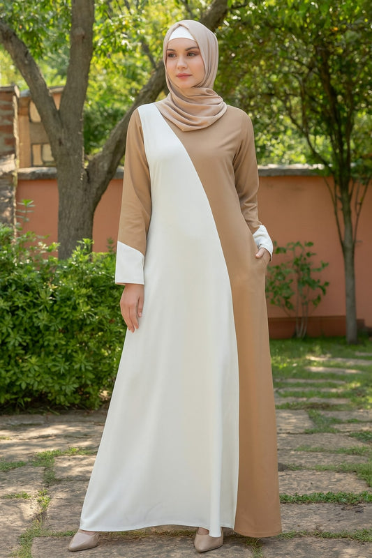 Woman wearing a beige and white dress standing outdoors with greenery in the background