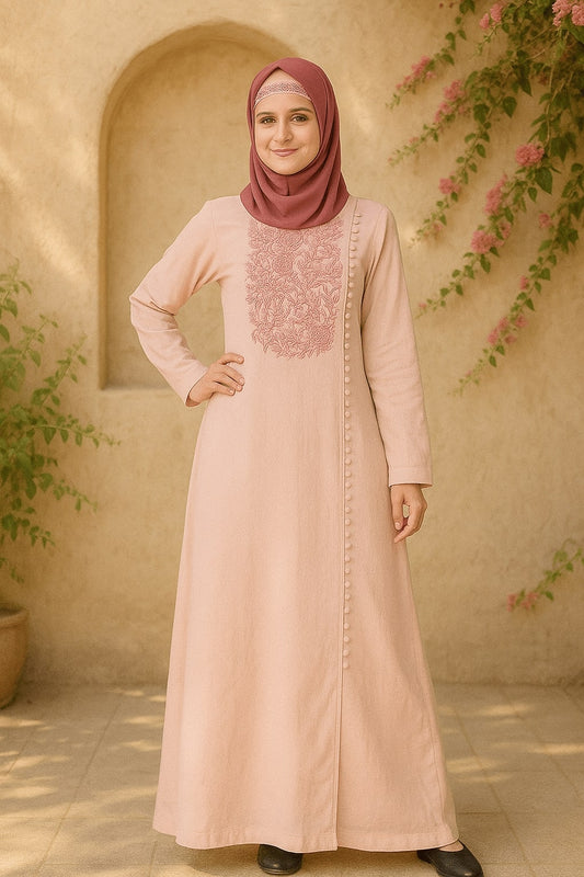 Woman wearing a long, light pink dress with intricate patterns in an outdoor setting.