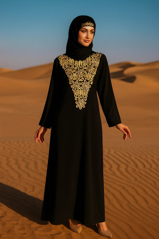 Woman in a black abaya with gold embroidery standing in desert sand dunes.