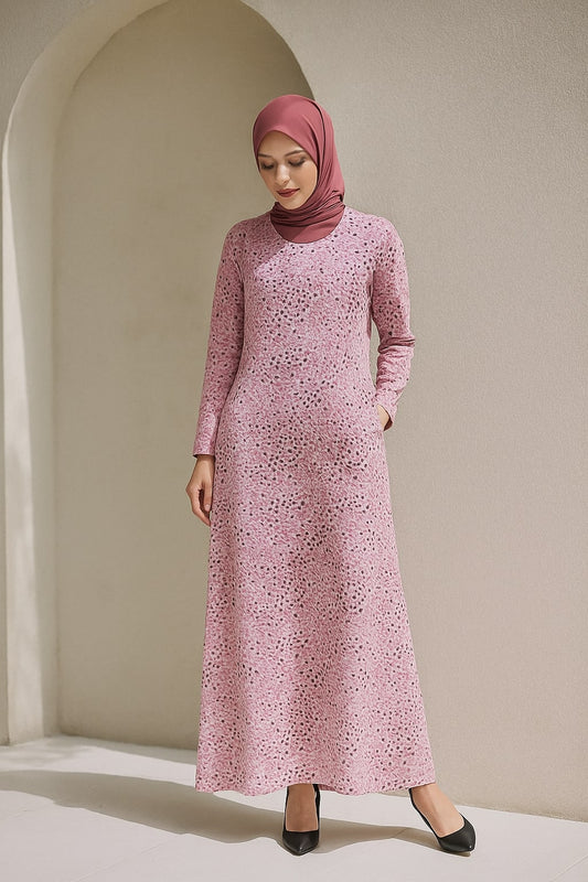 Woman wearing a pink patterned dress and hijab standing against a beige wall.