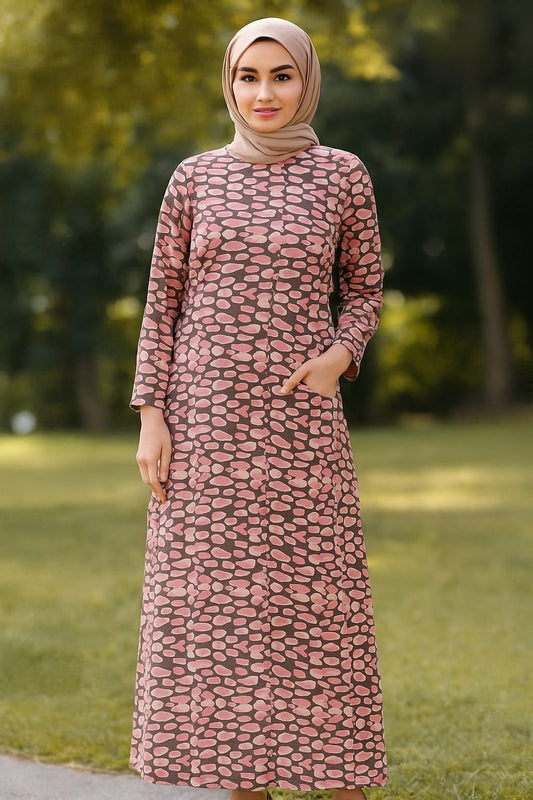 Woman wearing a pink patterned dress and hijab standing outdoors with greenery in the background
