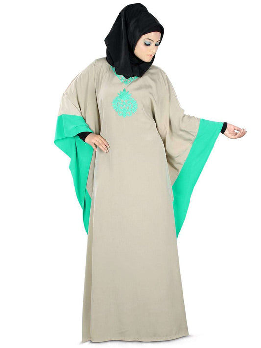 A woman wearing a beige and green kaftan with embroidery at the front, a 'V' neckline, and an adjustable belt at the waist.