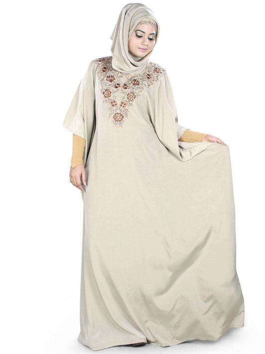A woman wearing a beige traditional Kaftan with floral embroidery and a round neckline.
